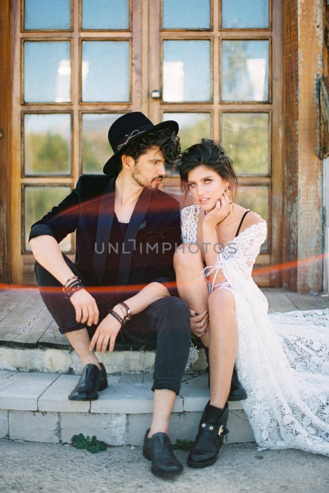 Groom turned his head to bride sitting on the threshold of a wooden house. High quality photo