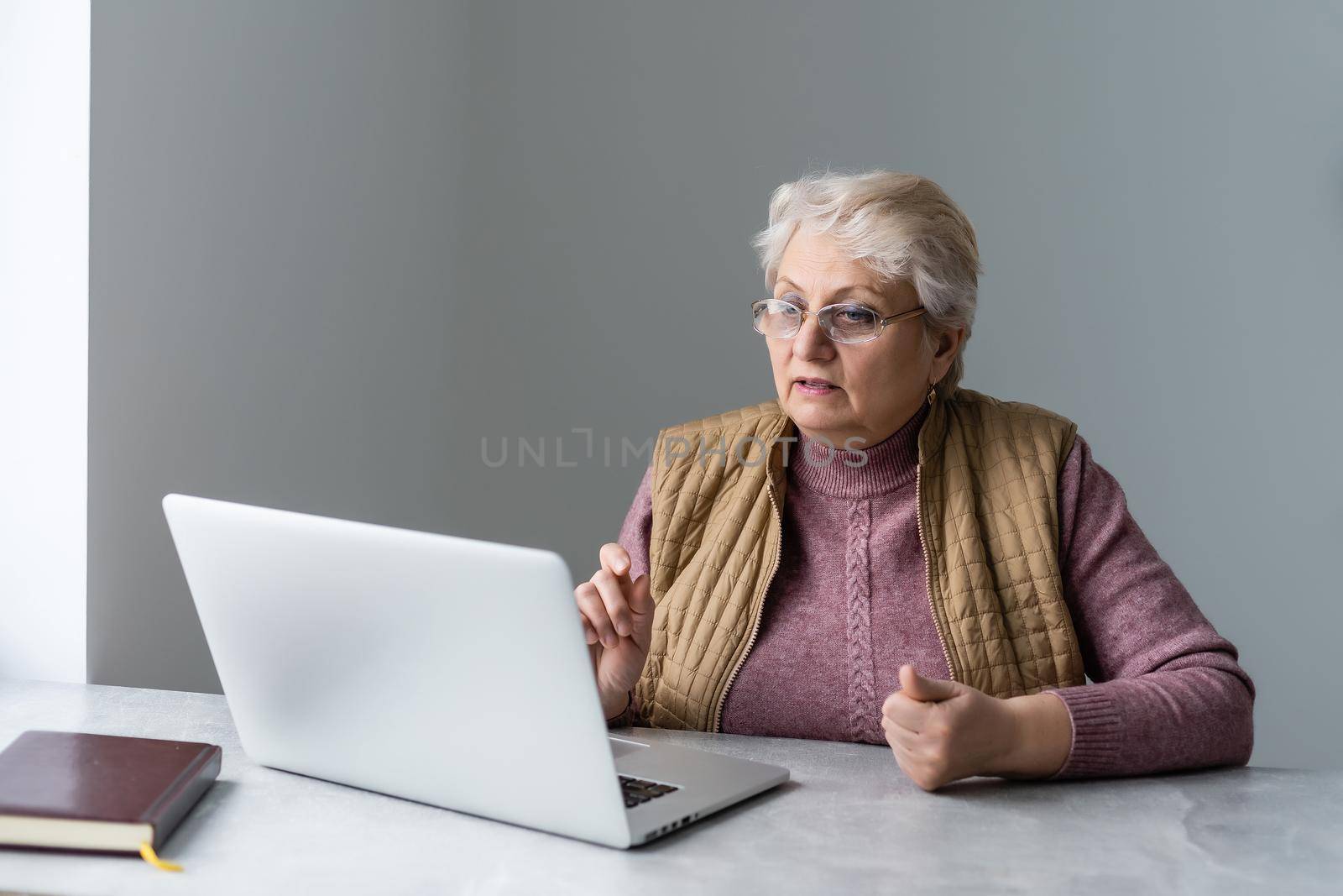 Serious mature older adult woman watching training webinar on laptop working from home or in office. 60s middle aged businesswoman taking notes while using computer technology.