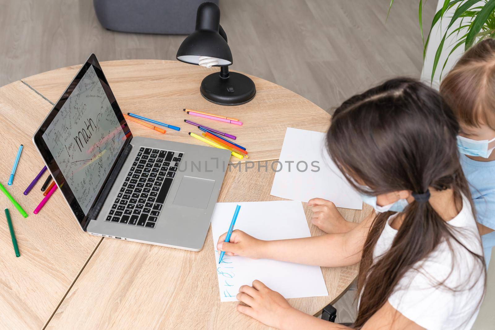 two little child girl studying online and working on laptop in wearing face mask.