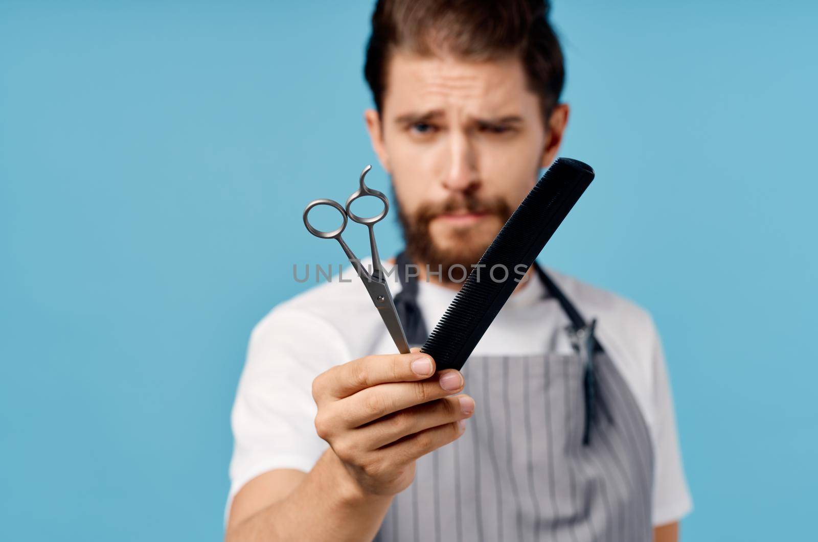 emotional hairdresser in gray apron with scissors and comb on blue background trendy hairstyle. High quality photo