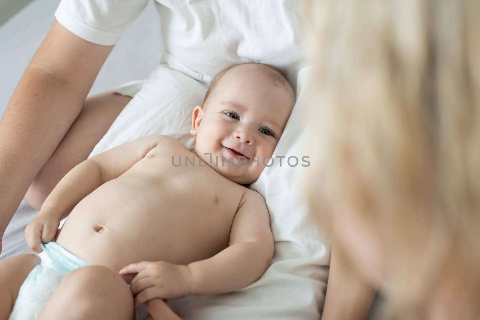 Adorable baby boy in white sunny bedroom. Newborn child relaxing in bed. Nursery for young children. Family morning at home. New born kid.