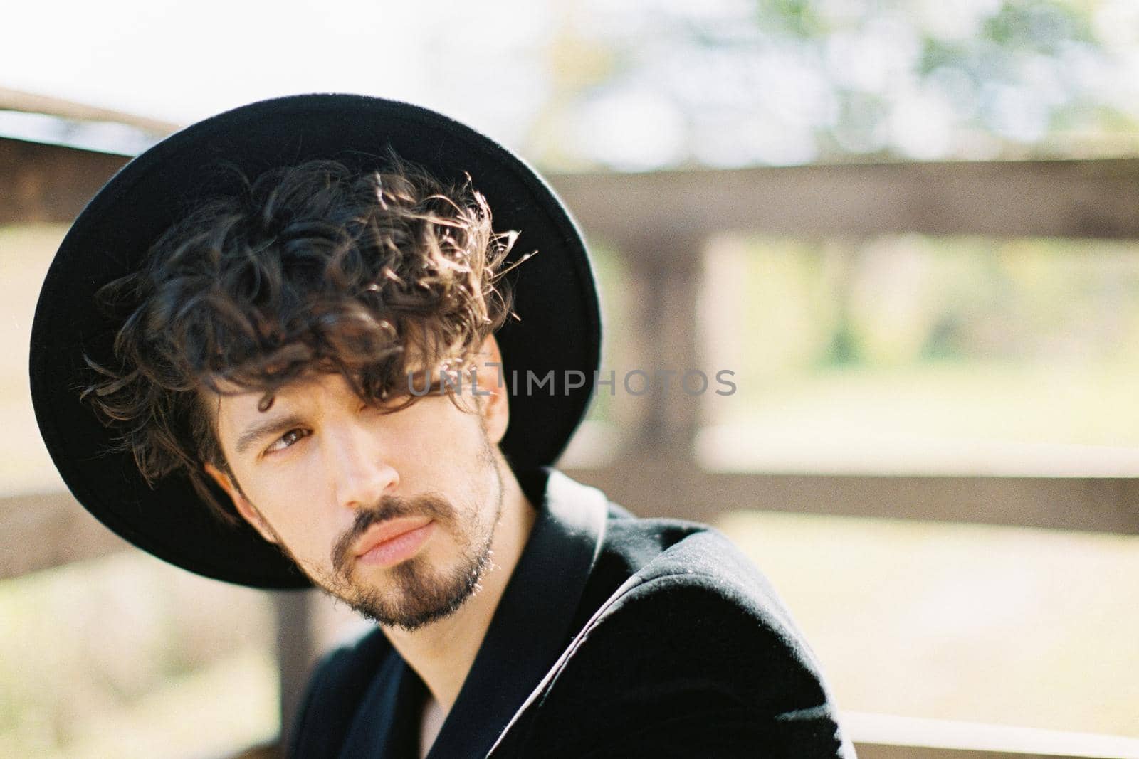 Young man in a black hat sits near a wooden railing. Portrait. High quality photo