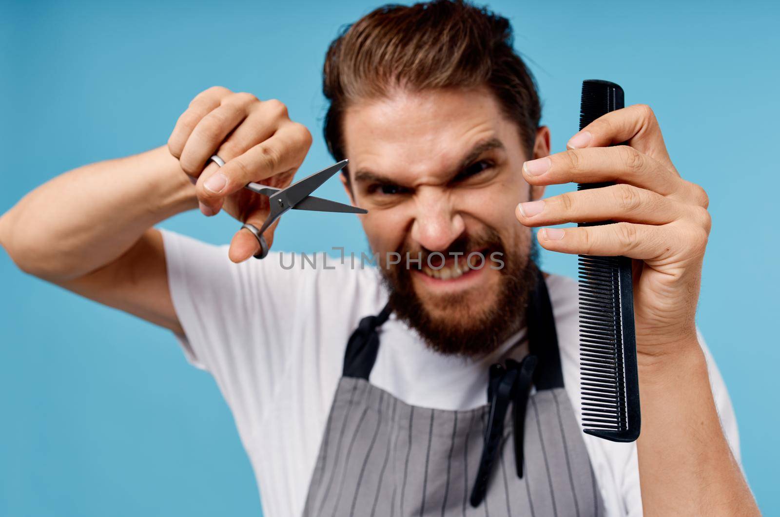 emotional male hairdresser with scissors and comb model beard gray apron cropped view. High quality photo