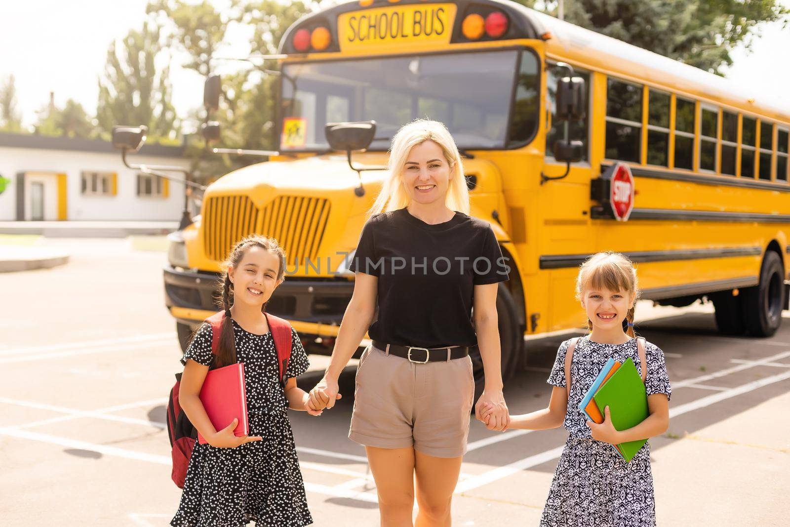 Back to school. Pupils of primary school near school bus. Happy children ready to study. little girls with mom going to bus by Andelov13