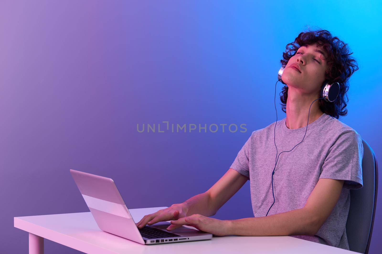 guy in headphones in front of laptop entertainment violet background. High quality photo