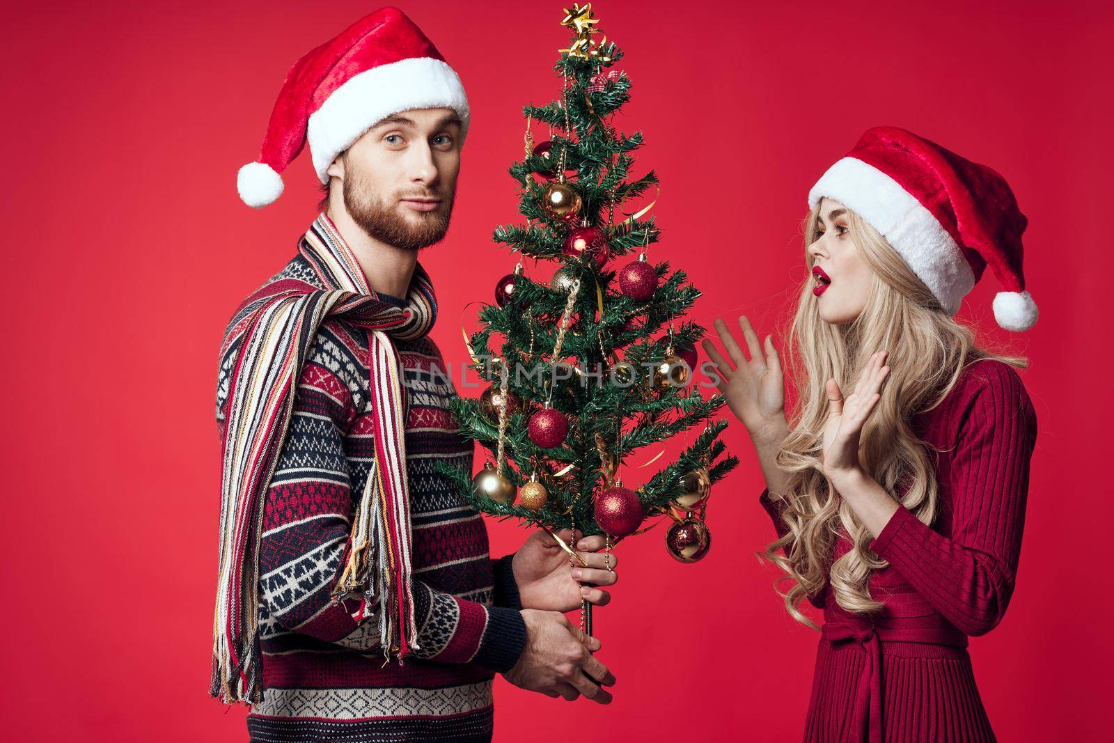 young married couple Christmas tree toys holiday joy red background by SHOTPRIME