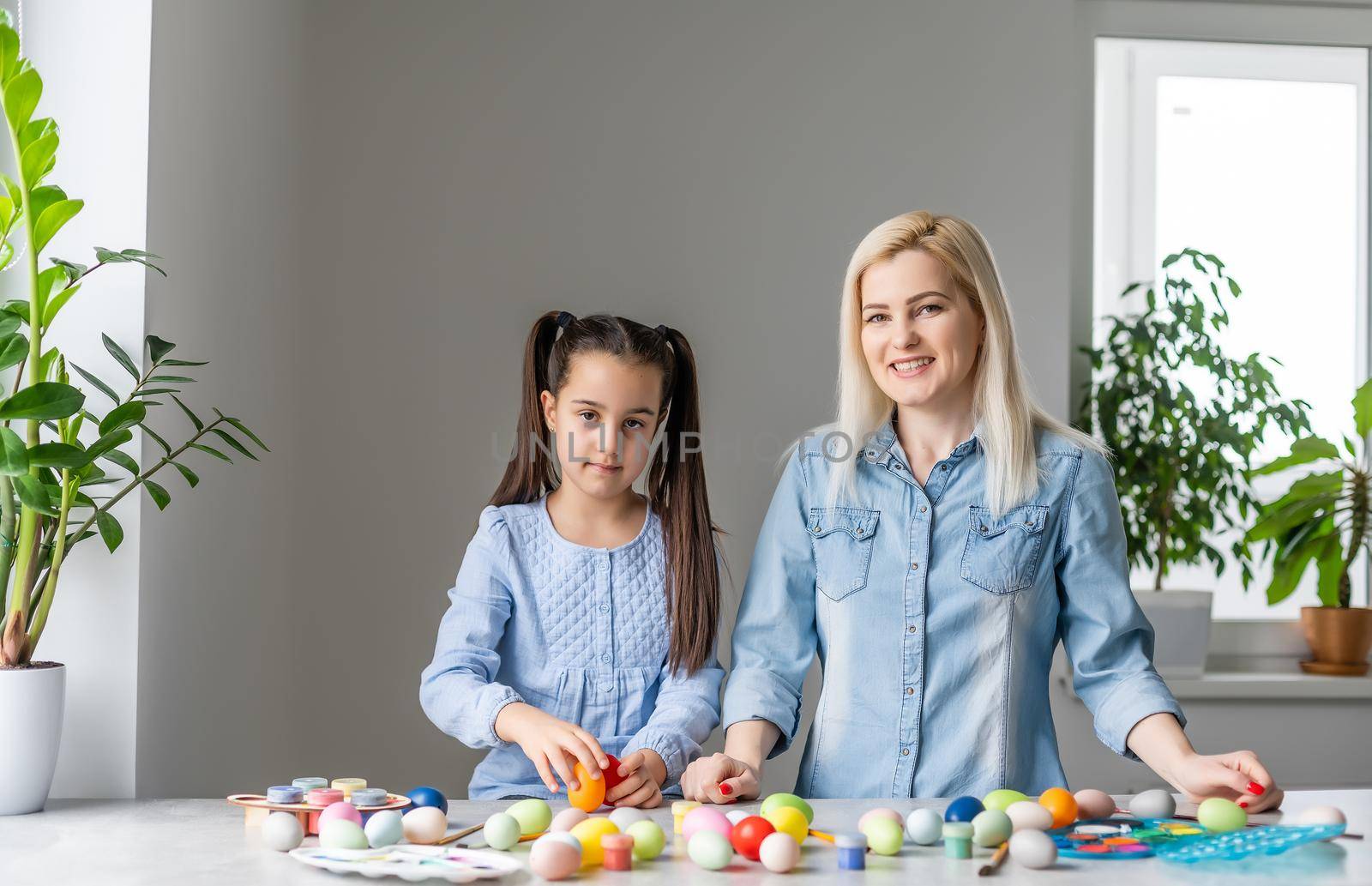 Happy easter. A mother and her daughter painting Easter eggs. Happy family preparing for Easter. Cute little child girl wearing bunny ears on Easter day. by Andelov13