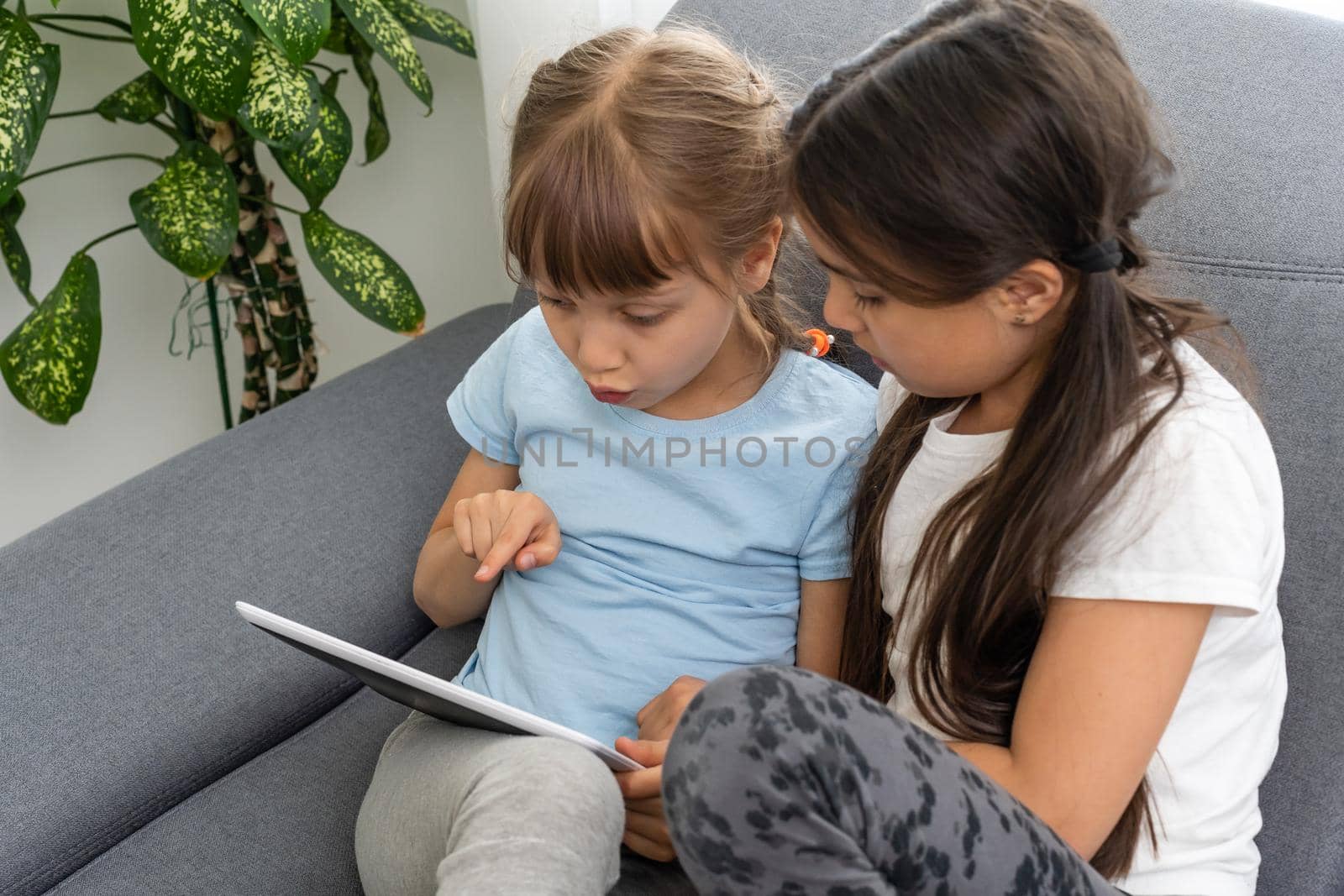 Closeup portrait of two smiling girls lying on couch and using tablet.