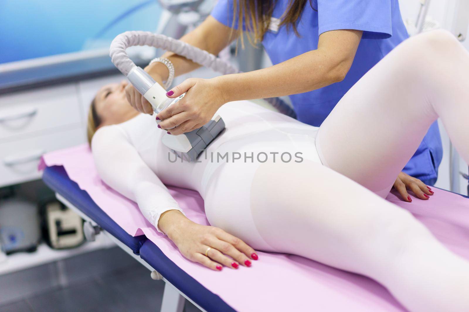 Middle-aged woman in special white suit having a anti cellulite belly massage with spa apparatus