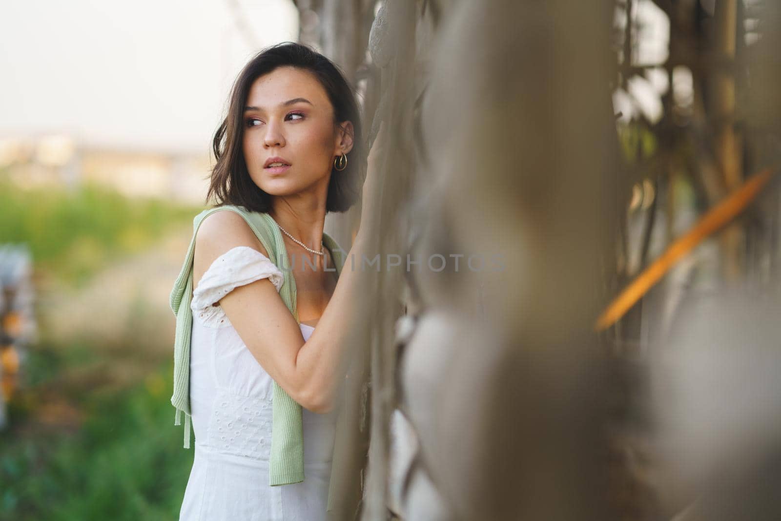 Pretty young Asian woman, posing near a tobacco drying shed, wearing a white dress and green wellies. Beauty and fashion concept