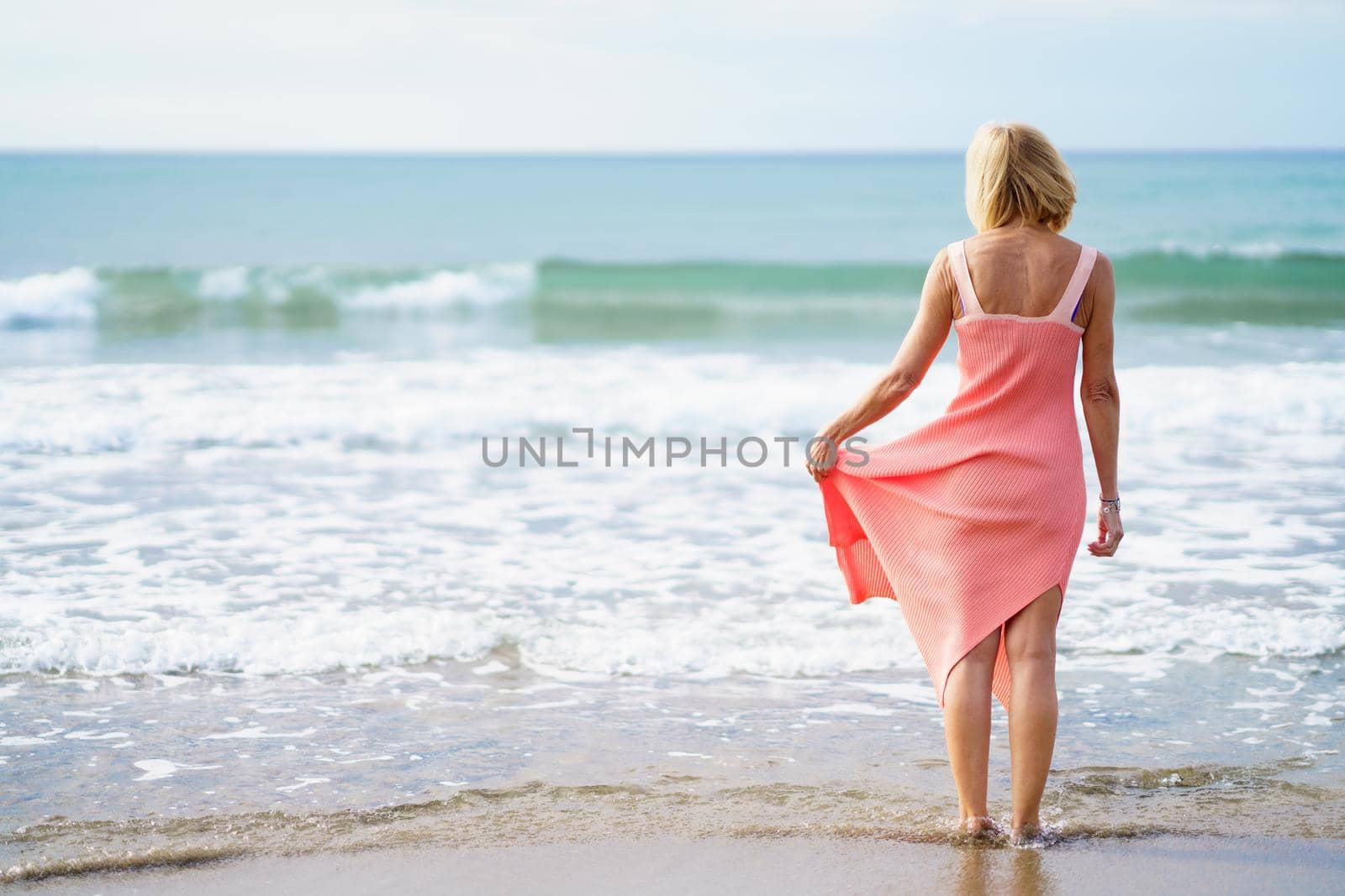 Older woman enjoying her free time looking at the sea from the shore of the beach.. Elderly female enjoying her retirement at a seaside retreat.