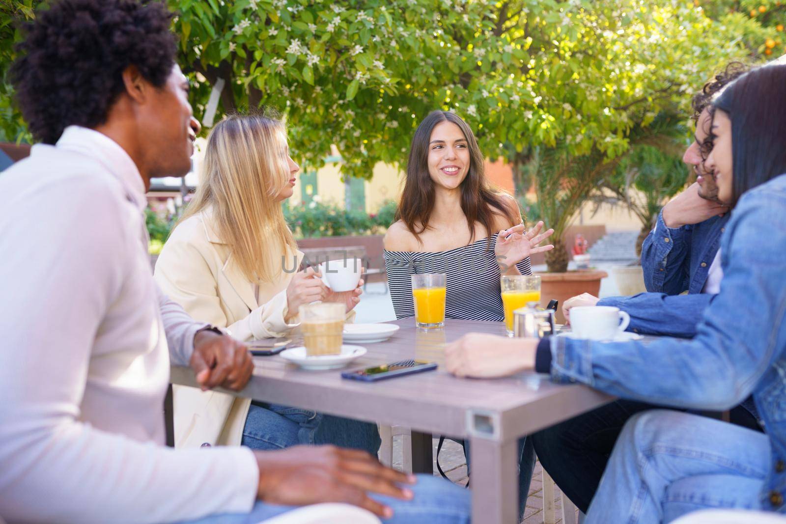 Multi-ethnic group of friends having a drink together in an outdoor bar. Young people having fun.