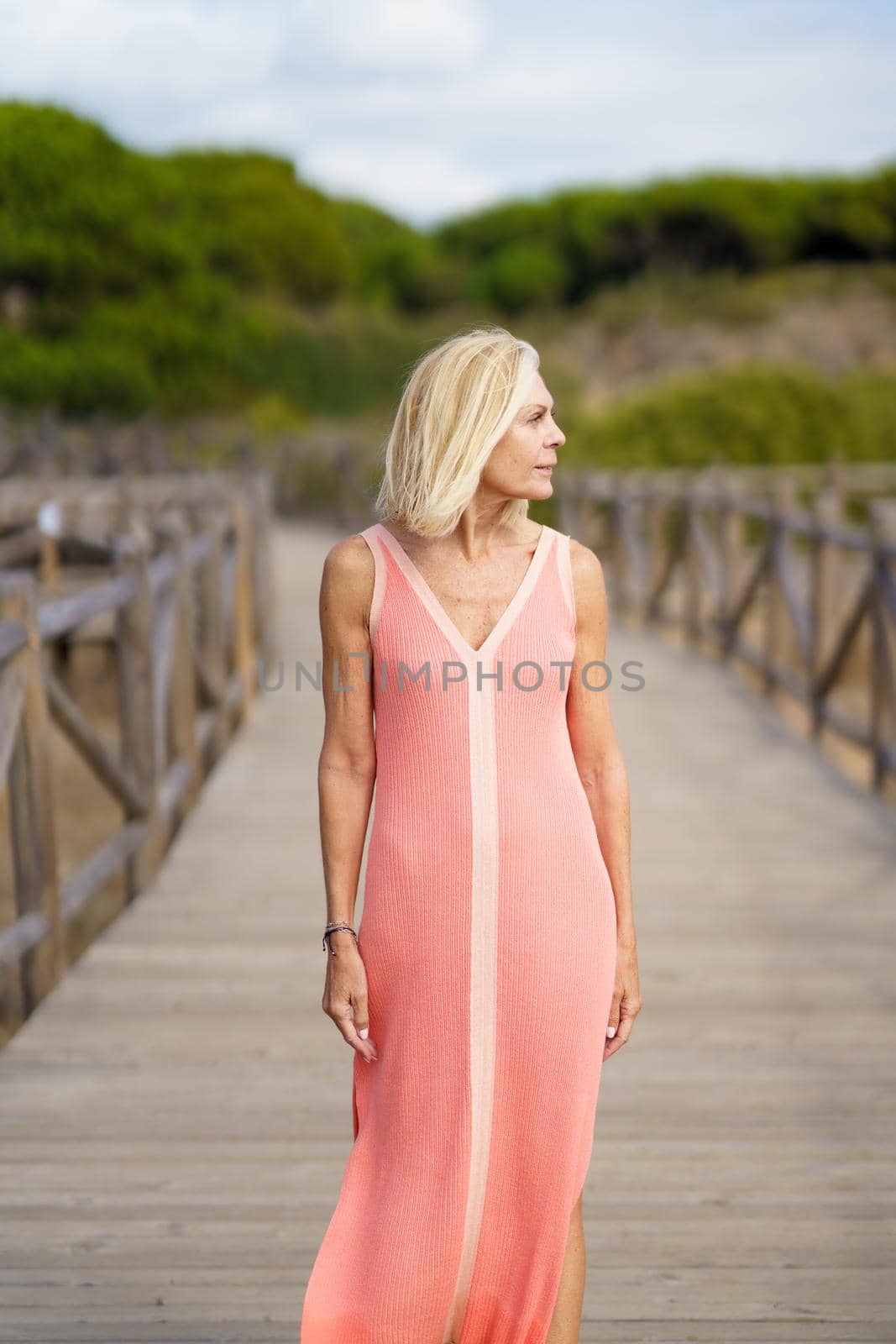 Beautiful mature female walking along a wooden path near the beach., wearing a nice orange dress. Elderly woman enjoying her retirement at a seaside retreat.