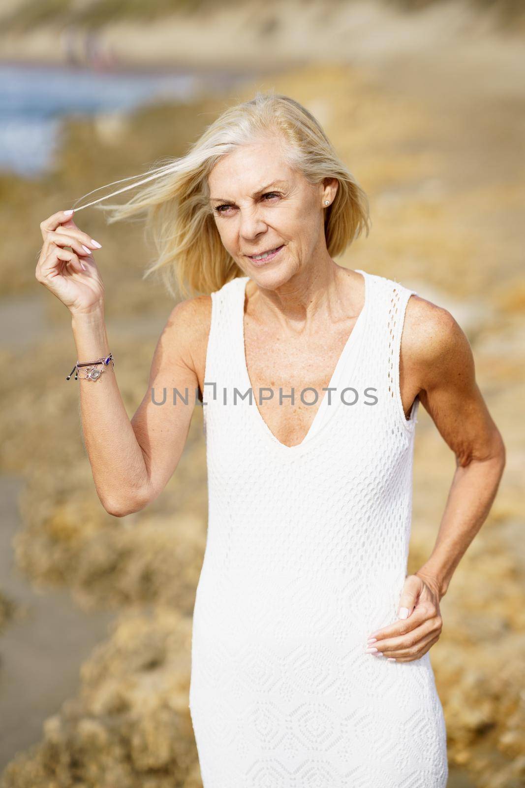 Mature woman walking on the beach. Elderly female standing at a seaside location by javiindy