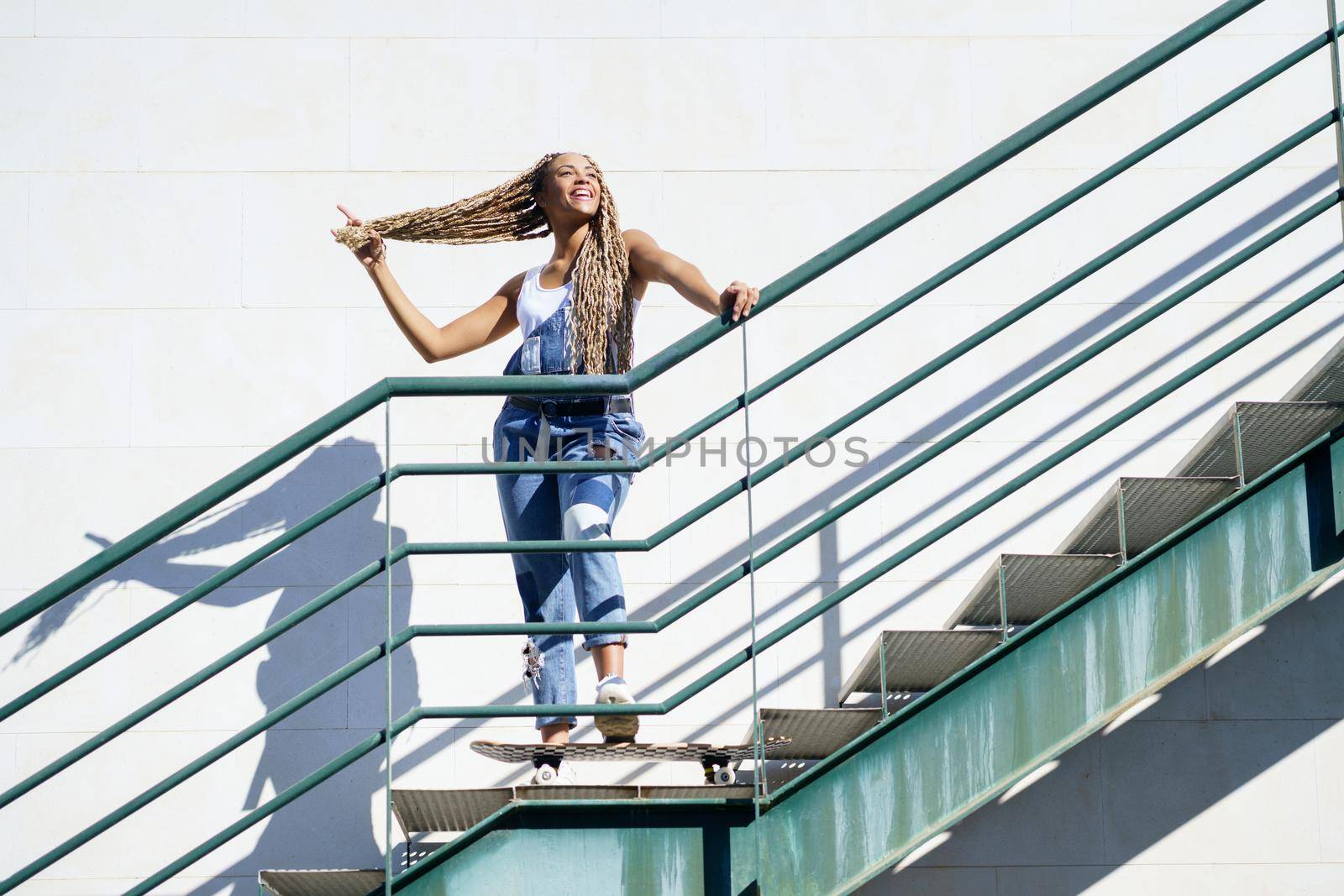 Beautiful young black girl on an urban staircase, holding her coloured braids. Typical African hairstyle.