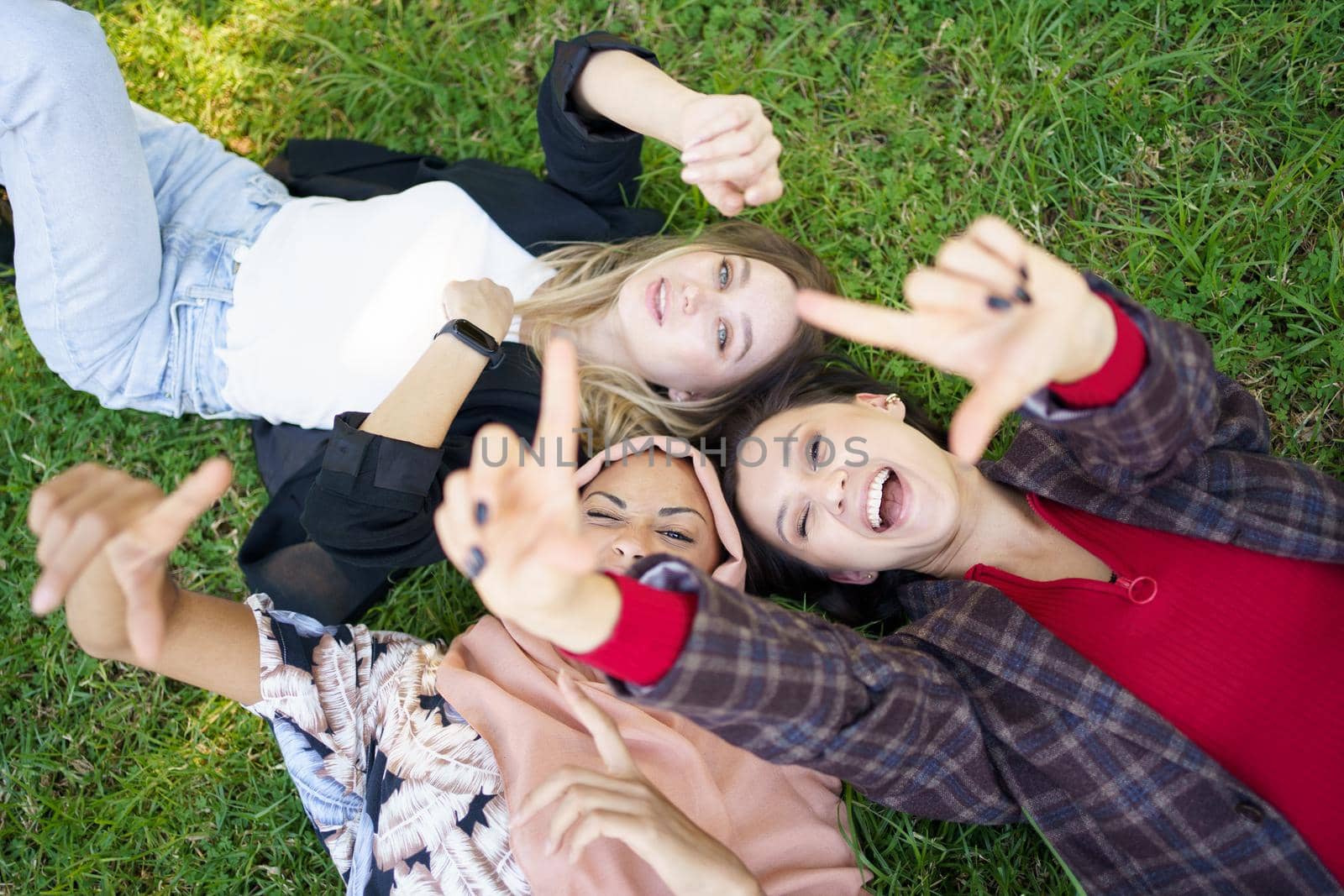 Cheerful ladies gesturing camera while lying on grass by javiindy