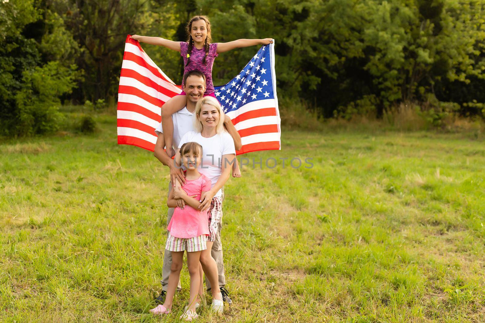 Patriotic holiday. Happy family, mother and daughters with American flag outdoors on sunset. USA celebrate independence day 4th of July. by Andelov13