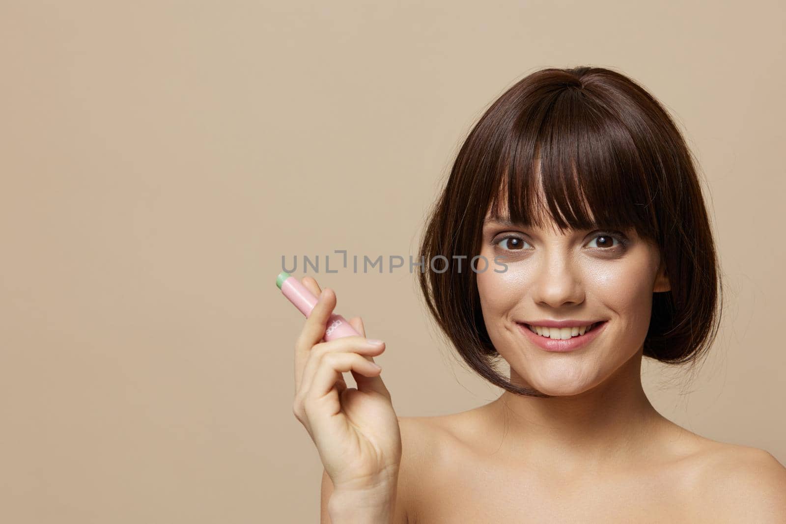 brunette makeup lip gloss near the face bare shoulders beige background. High quality photo