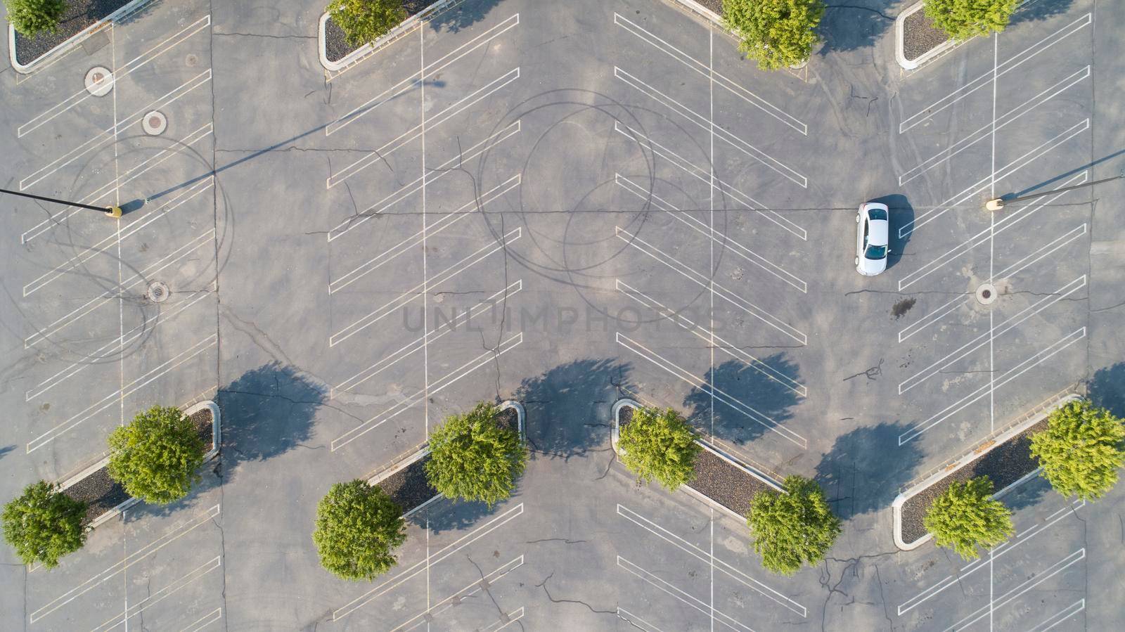 aerial view of a single car driving through an empty parking lot