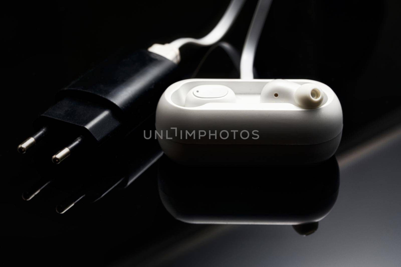 White wireless headphones plugged into charging station on a black background by vizland