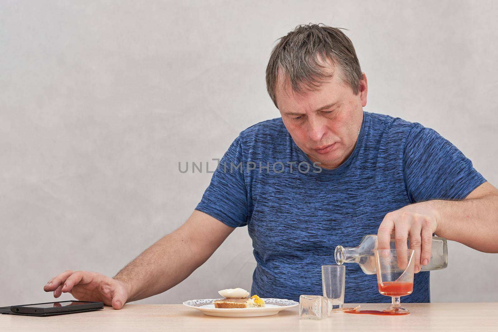 A drunkard sitting at a table pours alcohol and works on smartphone on the phone by vizland