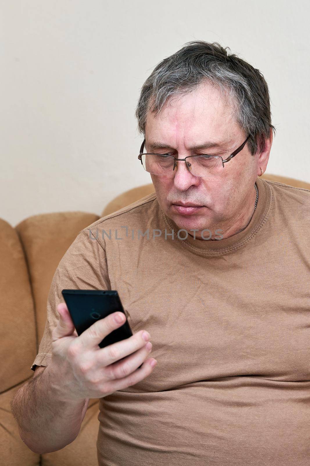 Senior citizen sitting on the couch understands the gadget, mastering smartphone by vizland