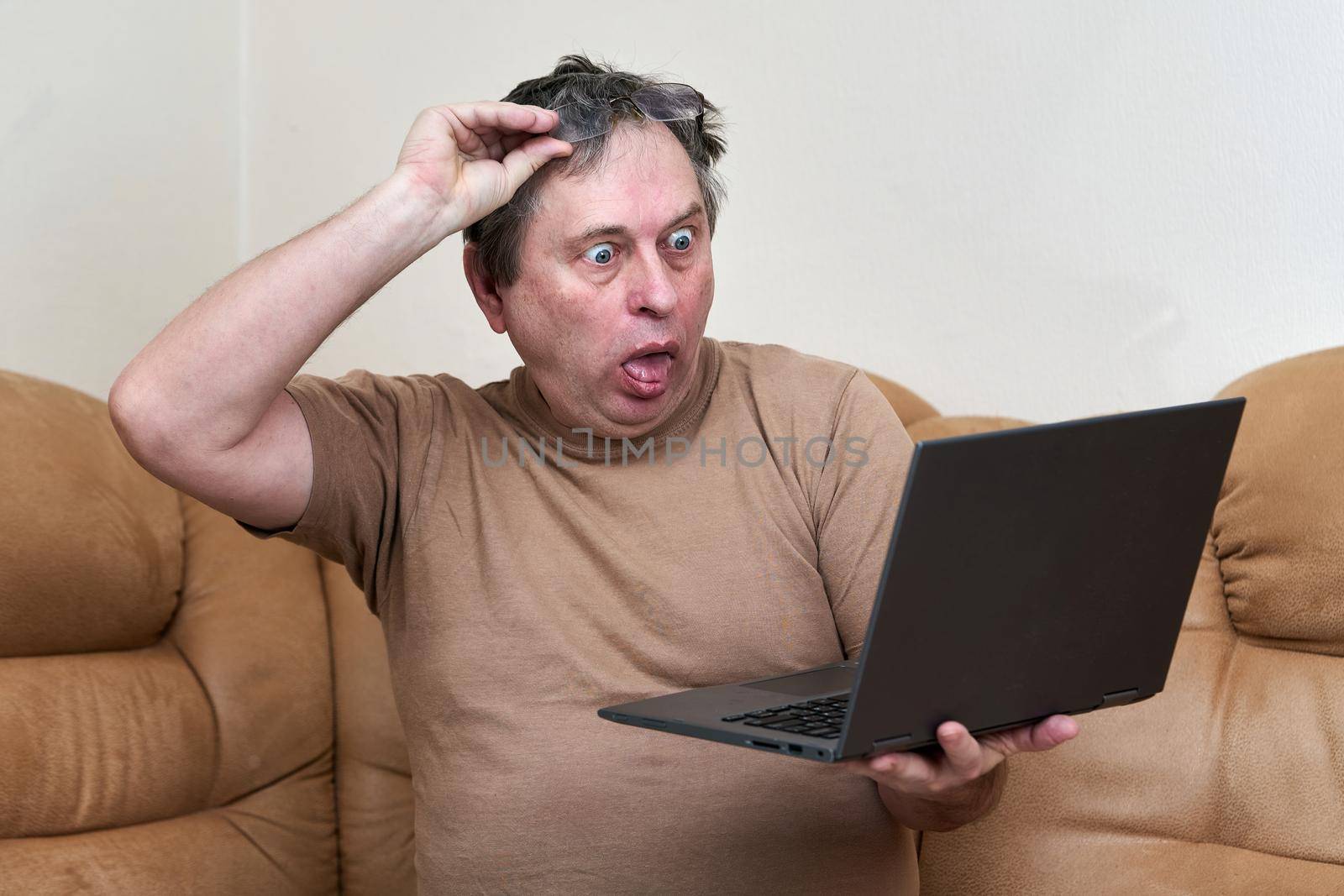 A man at the age of sitting on Devani looks through the news on a laptop. The man stuck out his tongue in surprise