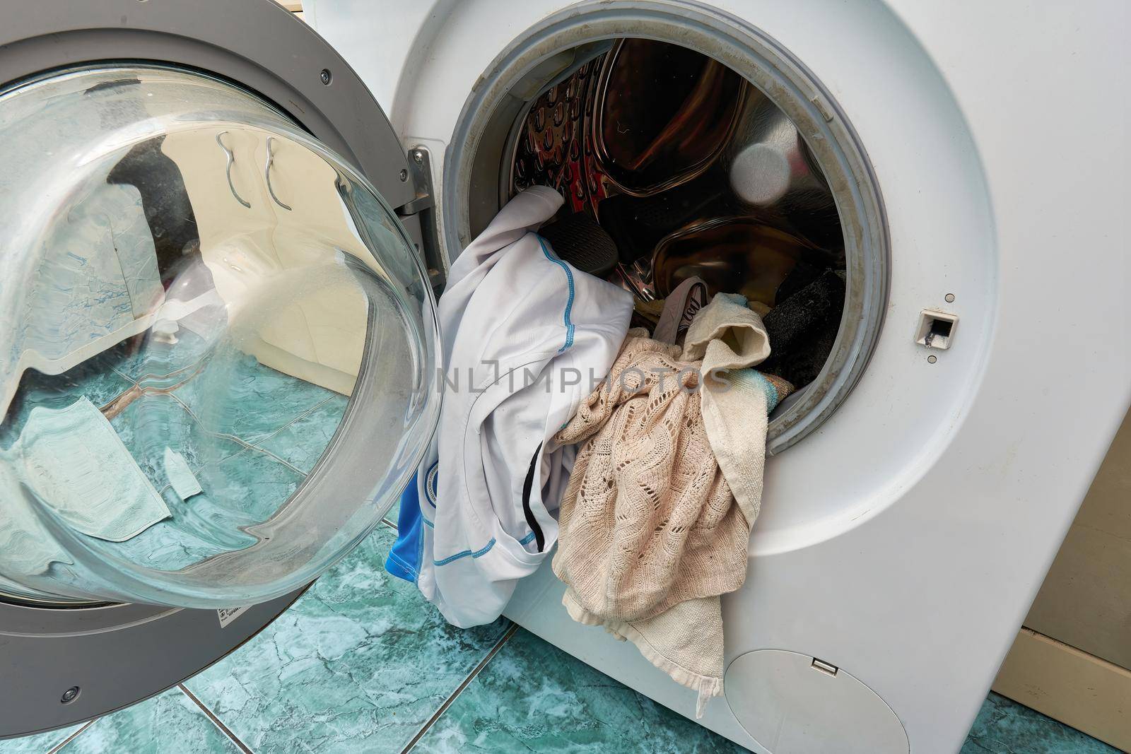 Washing machine with an open door and dirty laundry placed in the washing drum, close up.