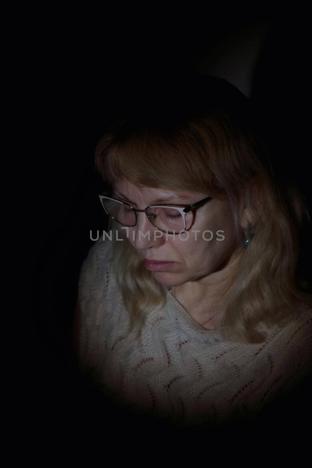 Face portrait of an aged woman wearing glasses with white long curly hair. Black background