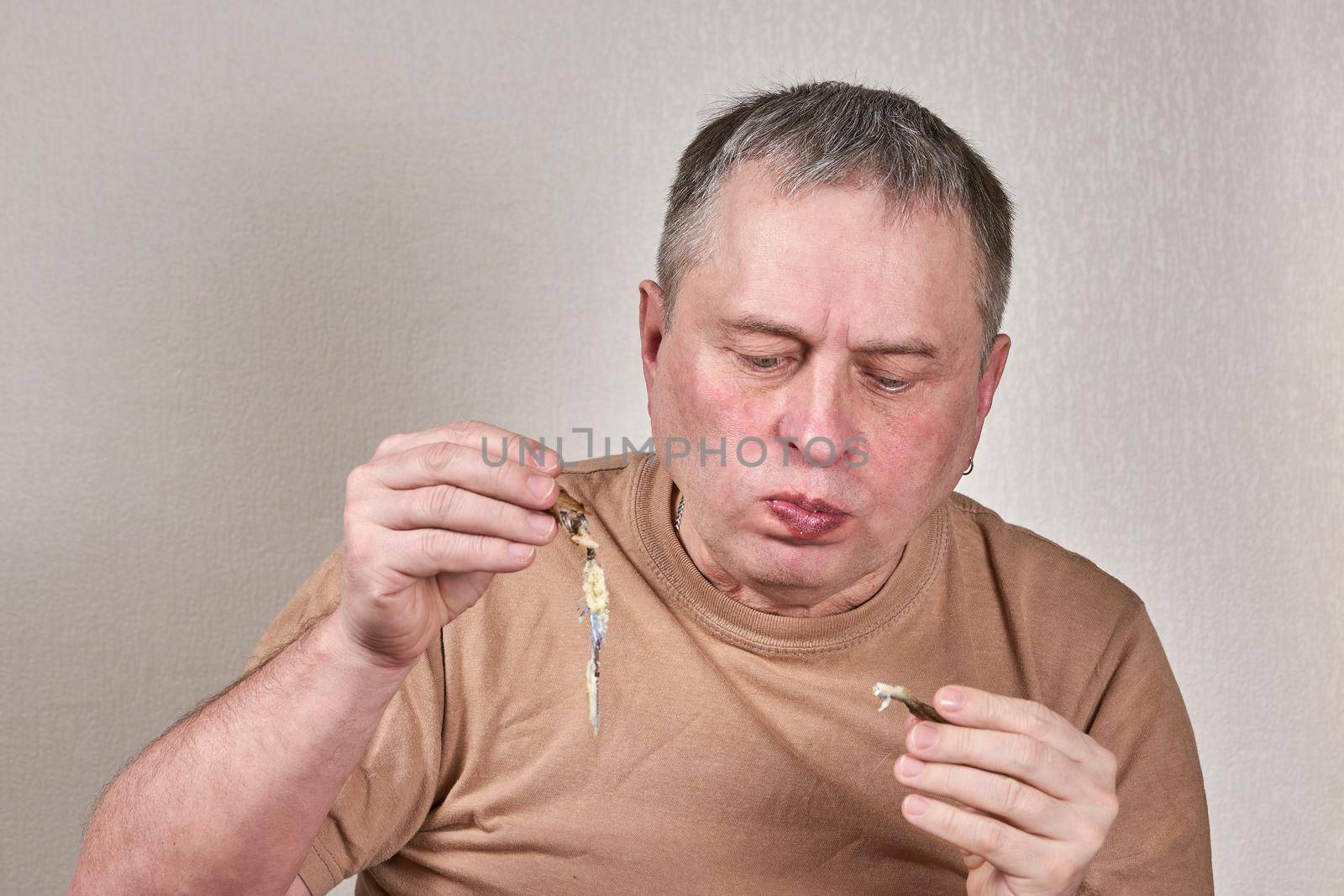 Man eating fried smelt fish holding fish with hands in front of face. Close up