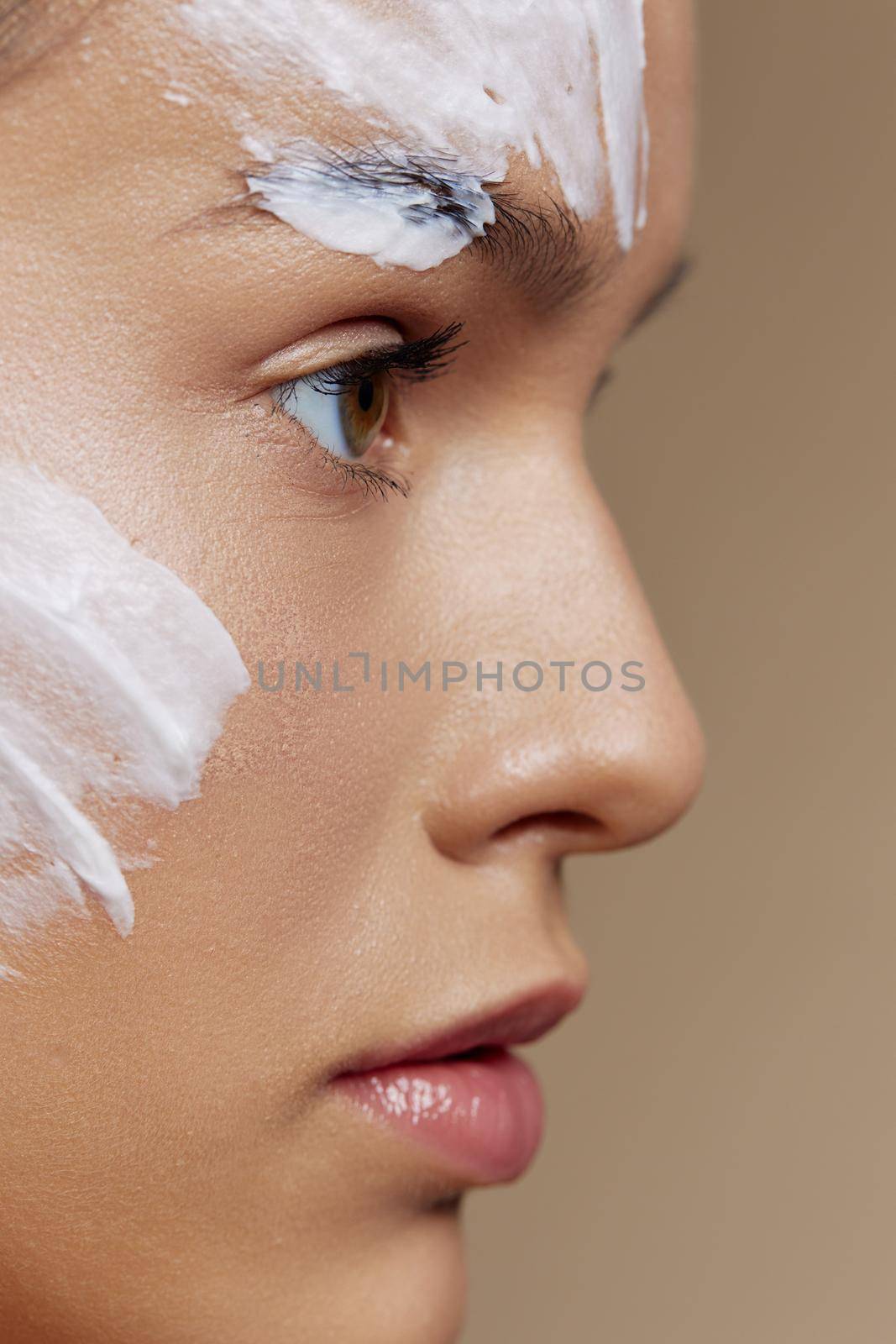 brunette applying a soothing face mask cosmetic beige background side view. High quality photo
