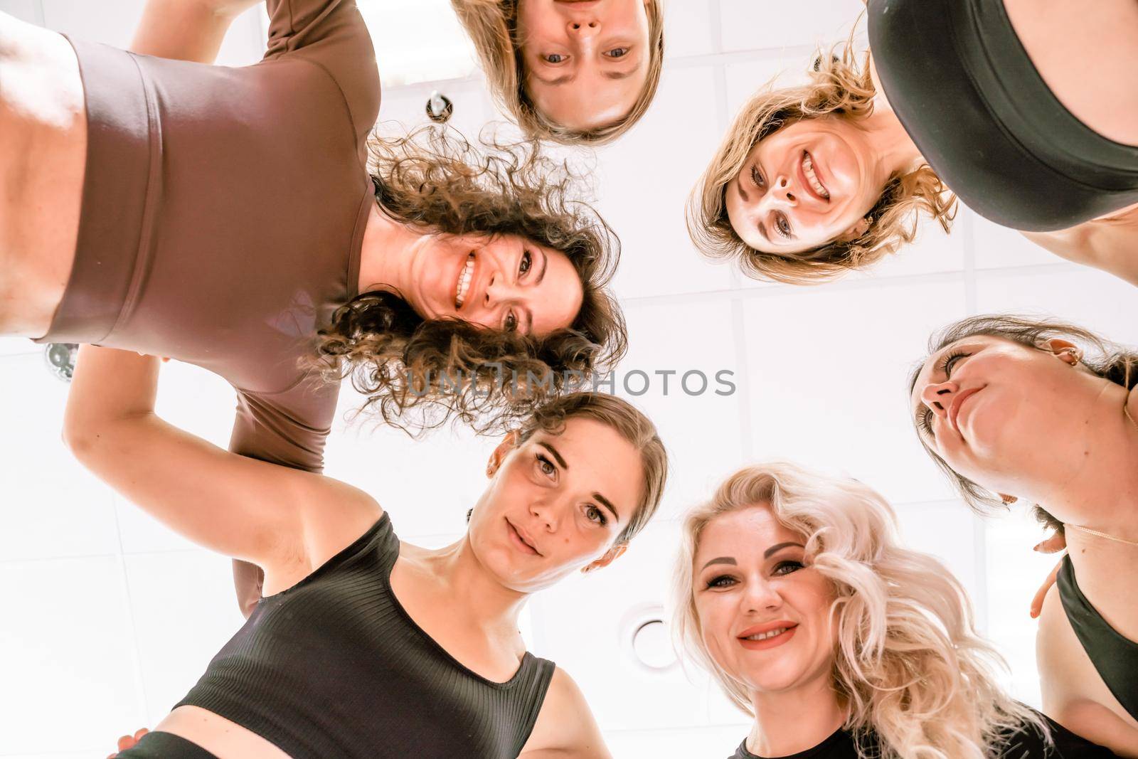 Low angle shot of smiling women looking at the camera, hugging, standing in a circle and doing team building by Matiunina