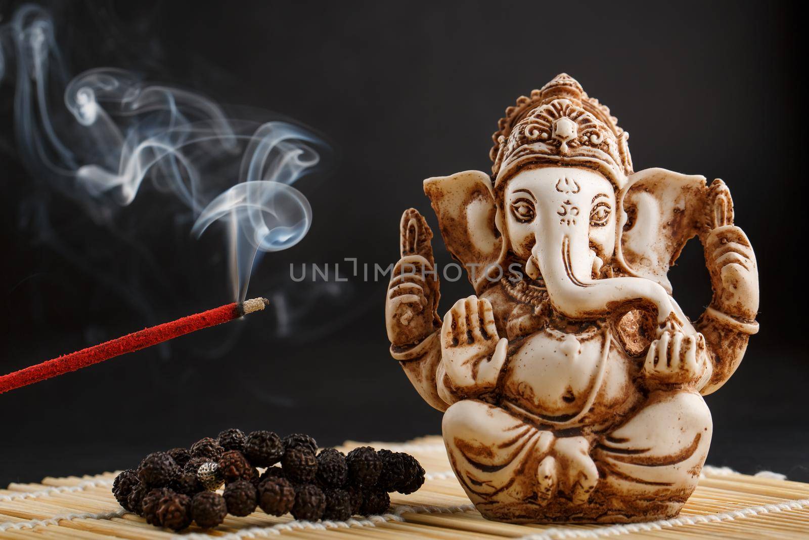 Ganesha on a black background. Statue and rosary with red smoldering incense stick Ganesha sahasranama