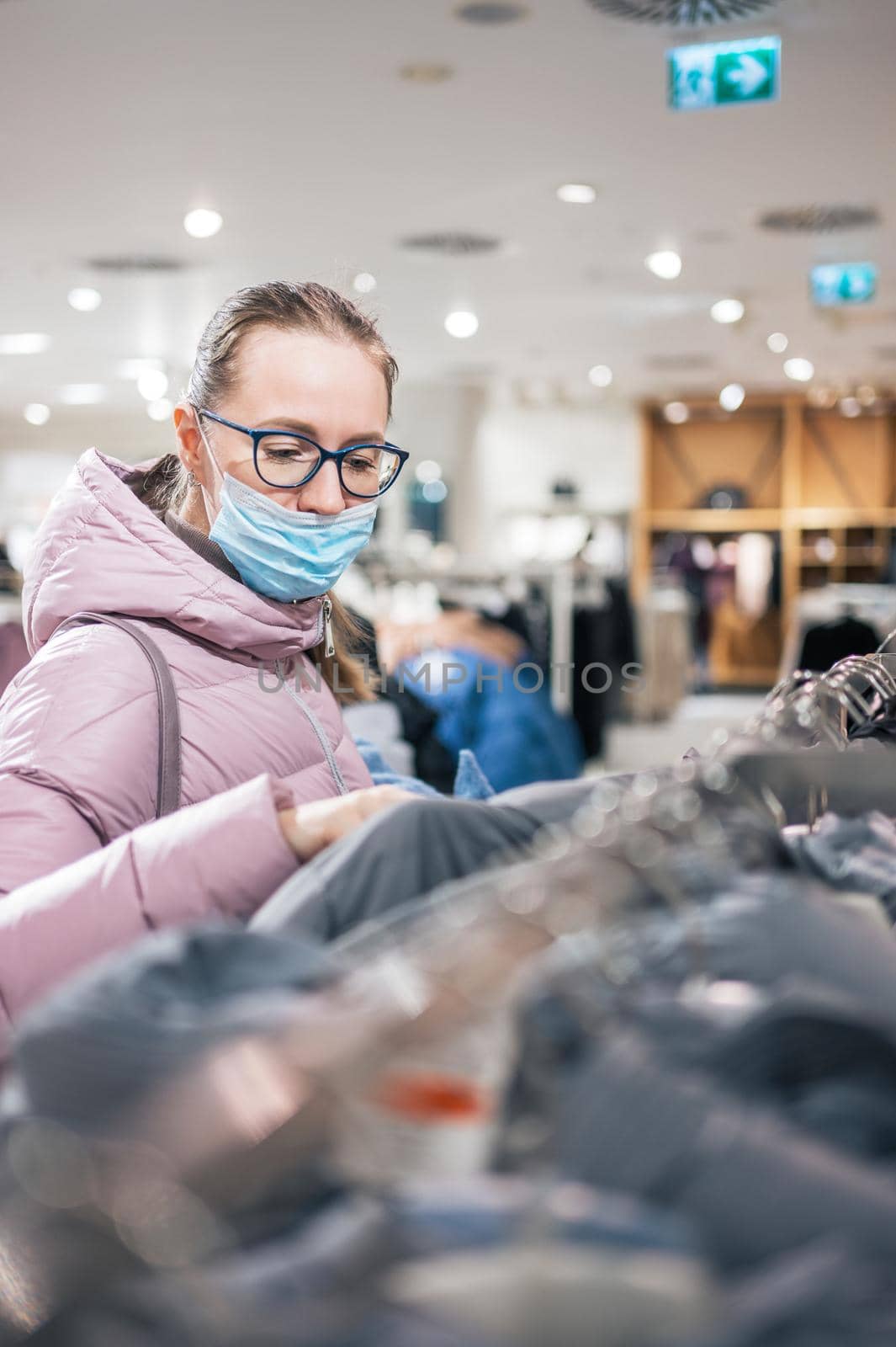Woman wearing protective face mask shopping clothes in retail shopping store. Concept of lifestyle during corona virus pandemic.
