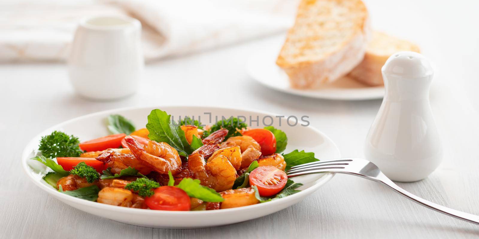 Fresh salad of shrimps, tomatoes, arugula and herbs on a white plate.