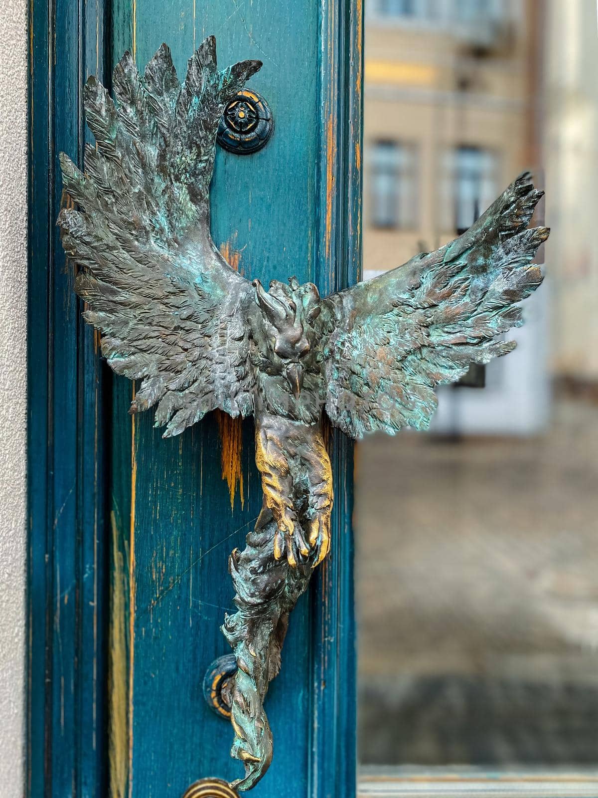 Turquoise wooden and glass entrance with antique door handle in the form of a bird. Unusual details of ornate door. Vintage iron door knob
