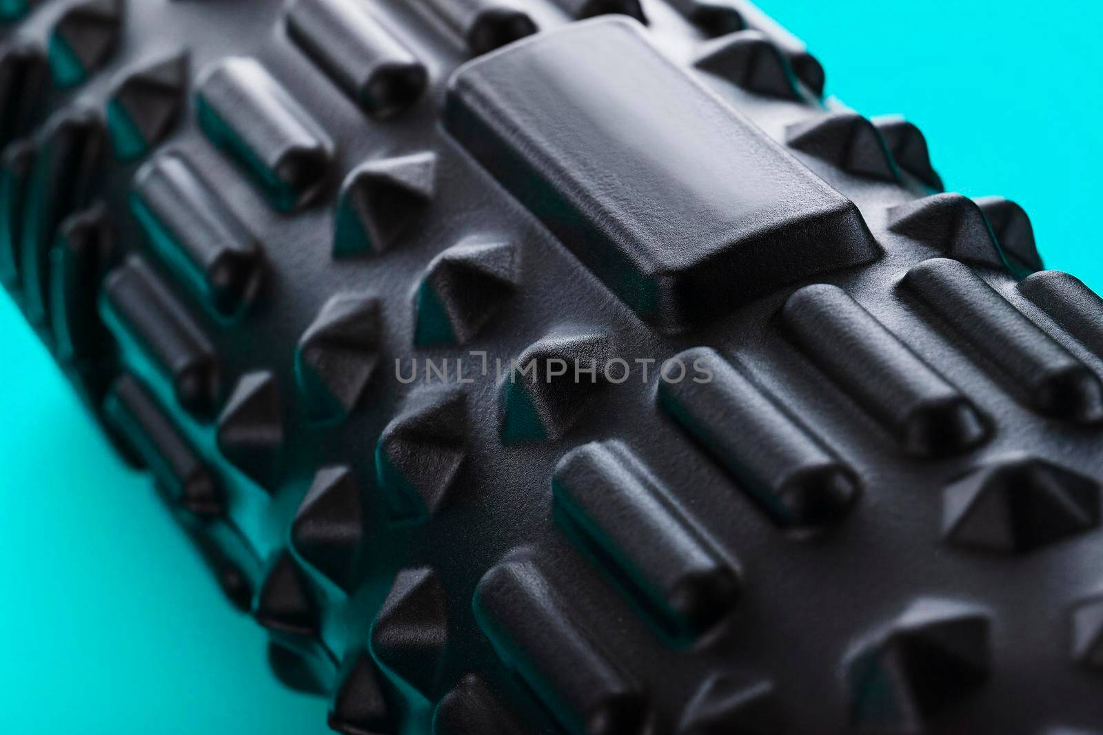 Black bumpy foam massage roller, body roller on blue background. For the mechanical and reflex effects on tissues and organs.