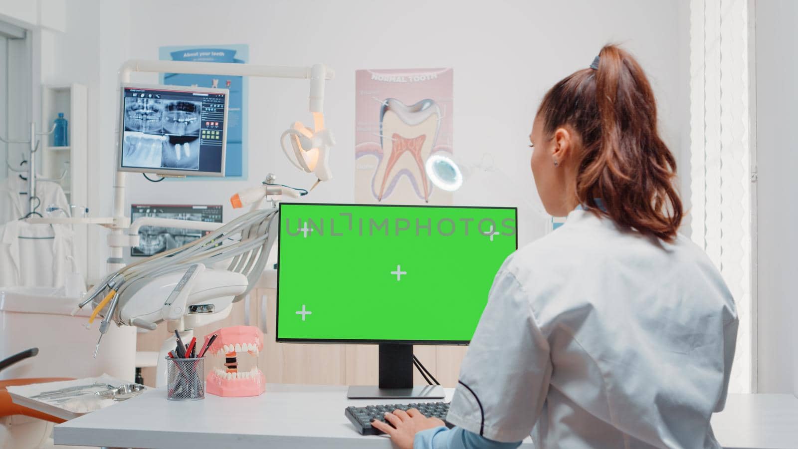Woman using keyboard and computer with green screen in dental cabinet for oral care. Dentist working with chroma key on monitor with isolated mockup template for dentition and dentistry