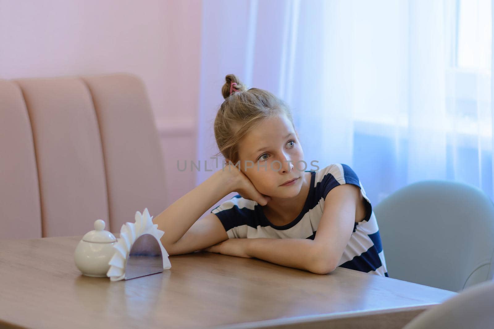 Teen girl 9 years sitting in a cafe at the table and waiting for the waiter with a menu to make an order