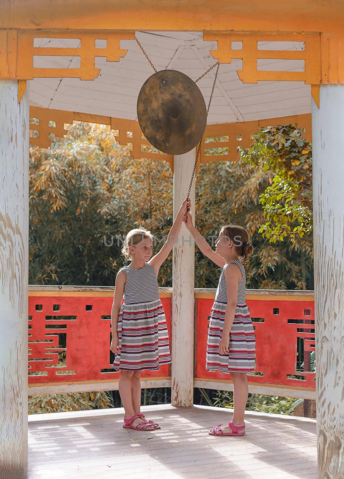 Two tween caucasian girls beating gong in classical chinese pavilion by andrew_donnikov