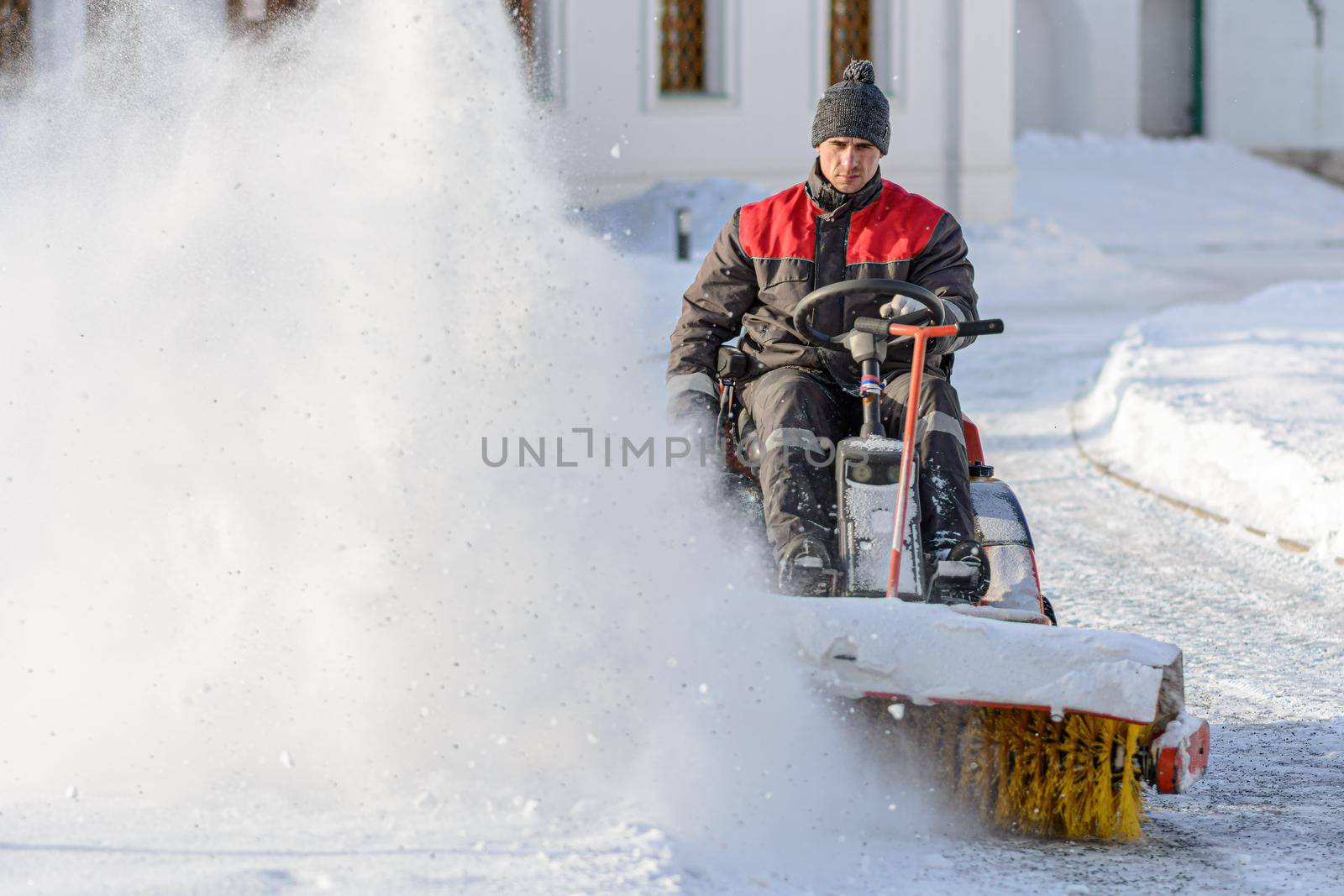 ISTRA, RUSSIA - FEBRUARY 05, 2021: Snow-removal work with rotating brush. Man with sweeping machine removing snow. Heavy precipitation and snow piles. Sunny winter morning