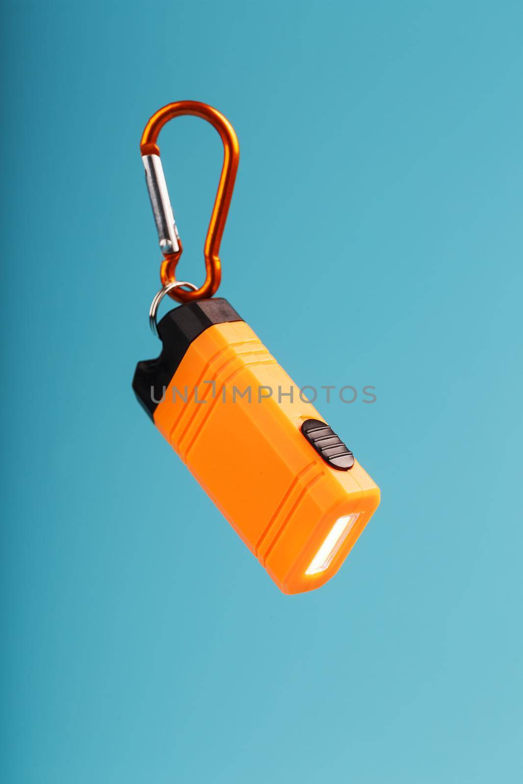 Orange led Flashlight with a carabiner on a blue background. LED lights in flight. Free space for text. Concept