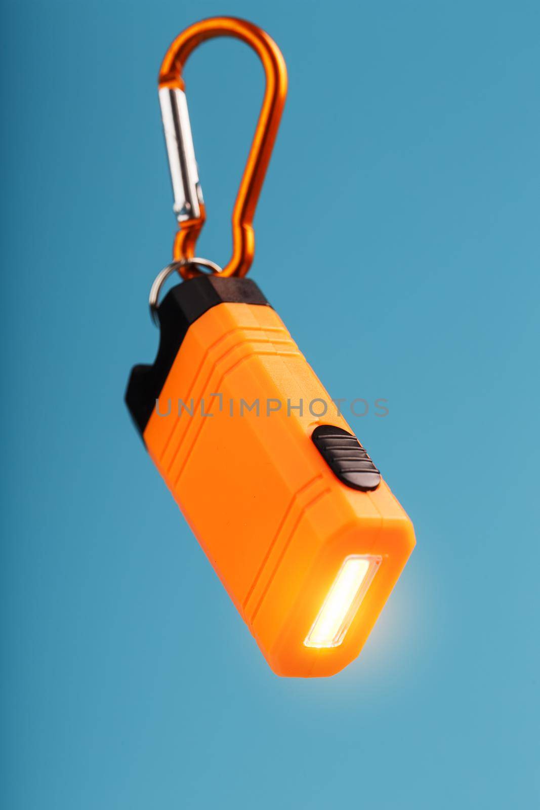 Orange led Flashlight with a carabiner on a blue background. LED lights in flight. Free space for text. Concept