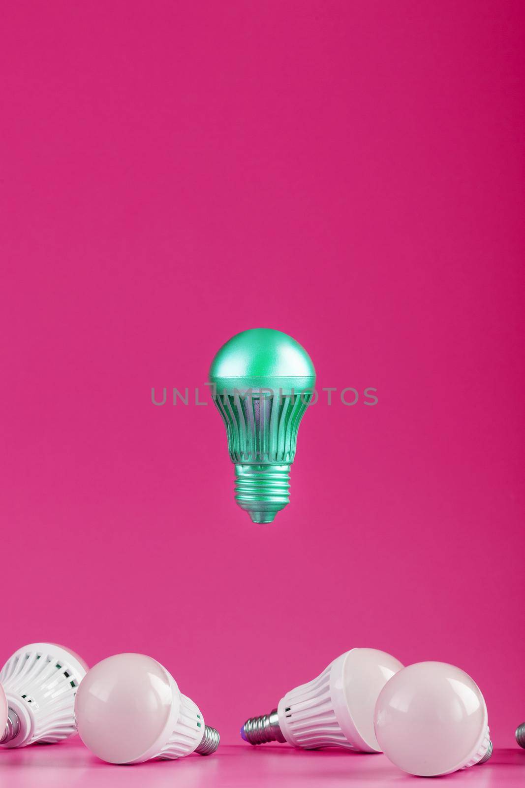 A special Light bulb hovers over simple, standard white light bulbs on a pink background. Minimalistic style with conceptual ideas. Be different