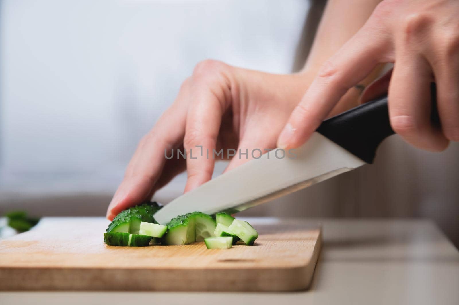 Close-up of female hands cutting cucumbers for a vegan salad. Home cooking healthy and wholesome food.