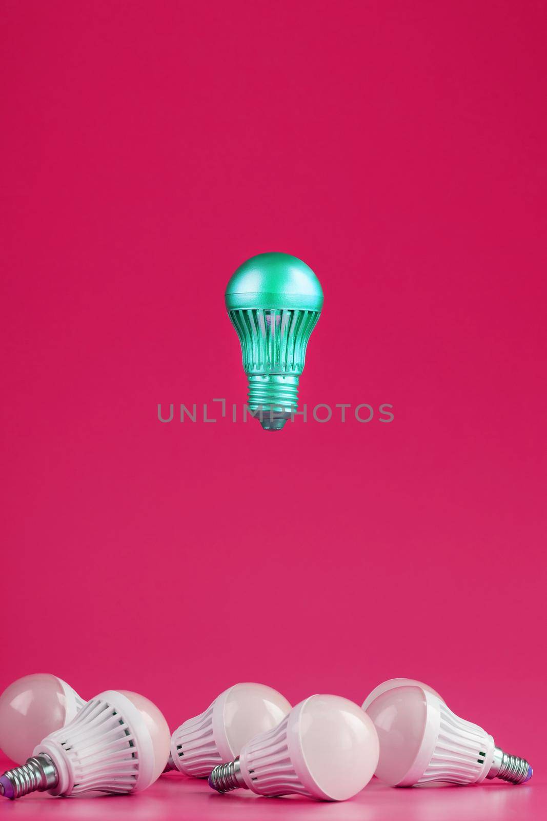 A special Light bulb hovers over simple, standard white light bulbs on a pink background. Minimalistic style with conceptual ideas. Be different