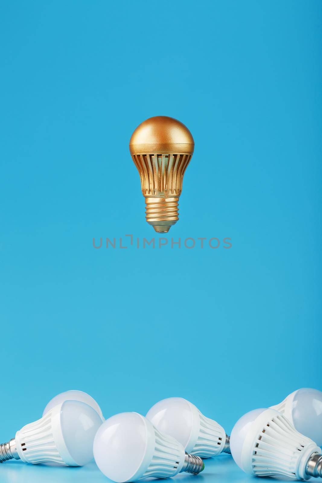 A prominent gold light bulb levitates above an environment of white led bulbs. The concept of an unusual idea and the contrast of surrounding rivals. Minimalism.