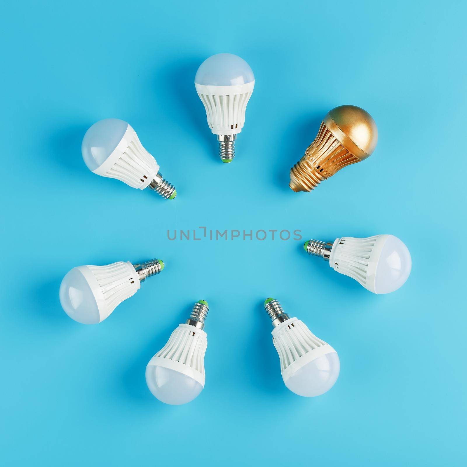 A Golden light bulb stands out in the circle of light bulbs of a ring of white lamps on a blue background. One original idea out of many is mediocre. Concept features, one in a crowd.