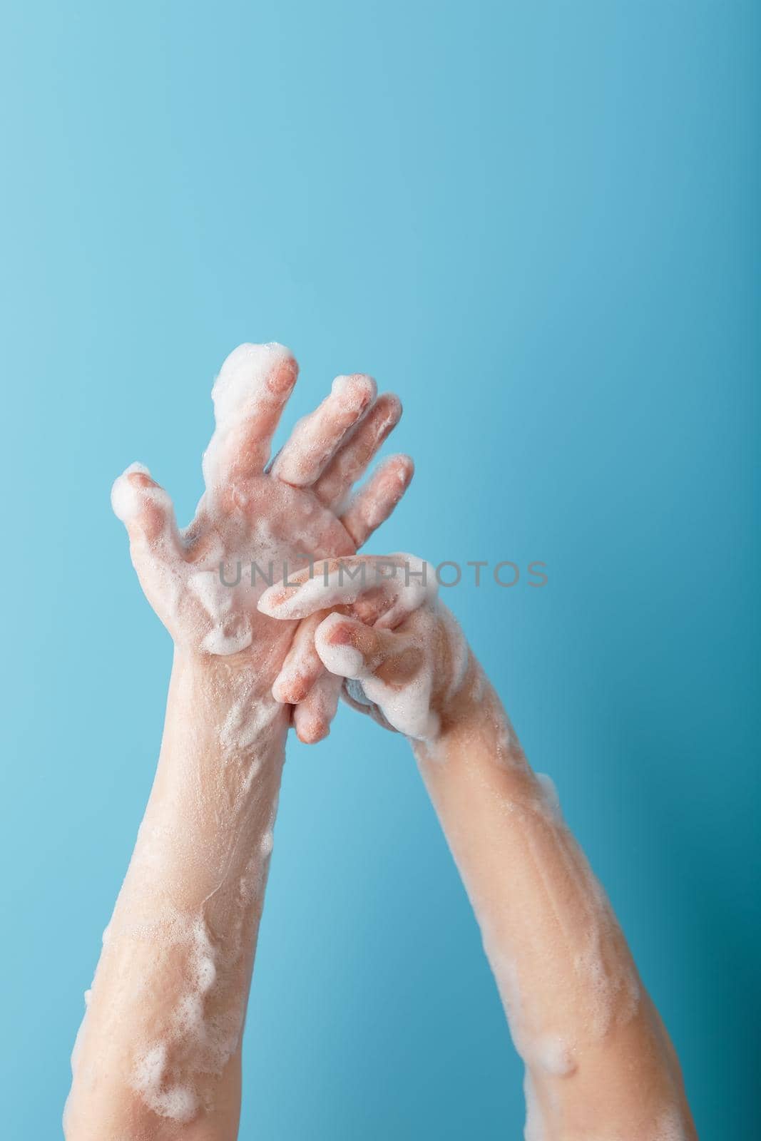 Children's hands in soap suds, on a blue background close-up, top view. Minimalistic concept of free space.