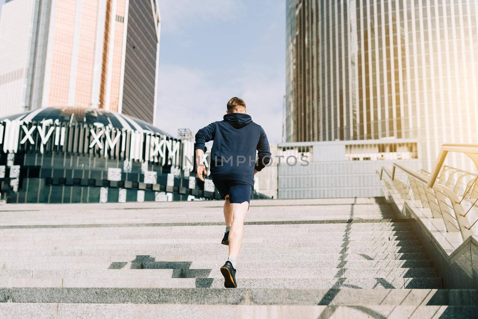 Young athlete man runner running up and down on city stairs in summer on morning run, background urban city street. Sports training. Fitness cardio workout in fresh air, walk outside.